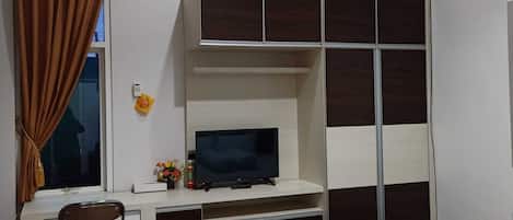 Un dormitorio con cama, escritorio con televisor, armario y ventana con cortinas.