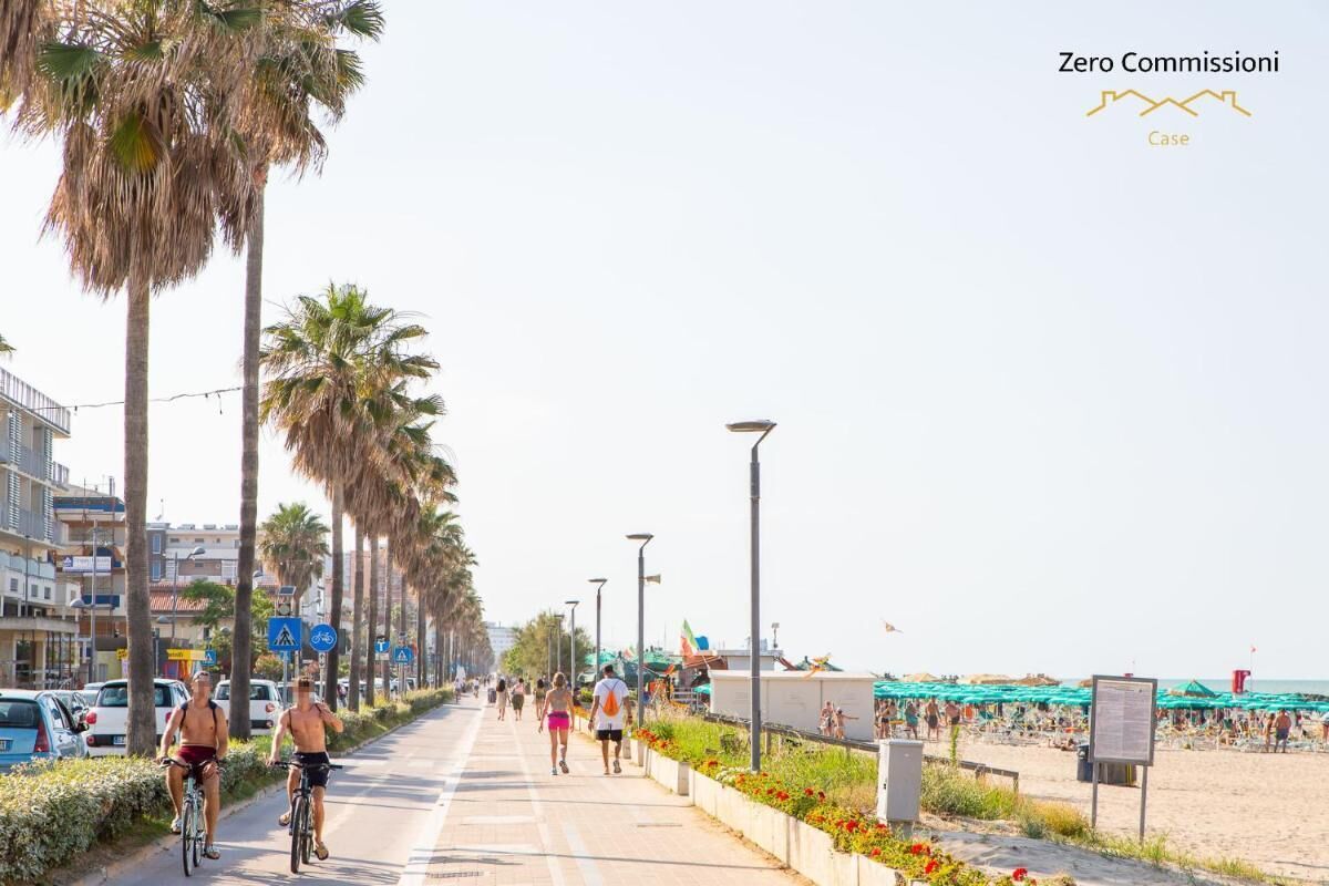 A coastal promenade with cyclists, a beach in the background, and a clear sky.
