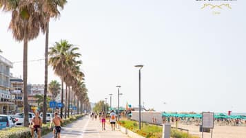 A coastal promenade with cyclists, a beach in the background, and a clear sky.