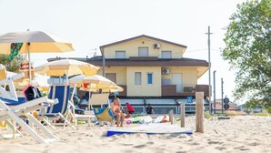A beach with sun loungers and umbrellas, a building with a balcony, and a lifeguard tower. - Palm Beach House - Sea and Beach View (Montesilvano)