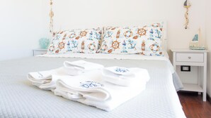 A neatly made bed with a white comforter and a pillow with nautical prints, a small bedside table with a decorative item, and a wall-mounted nightstand. - Palm Beach House - Sea and Beach View (Montesilvano)