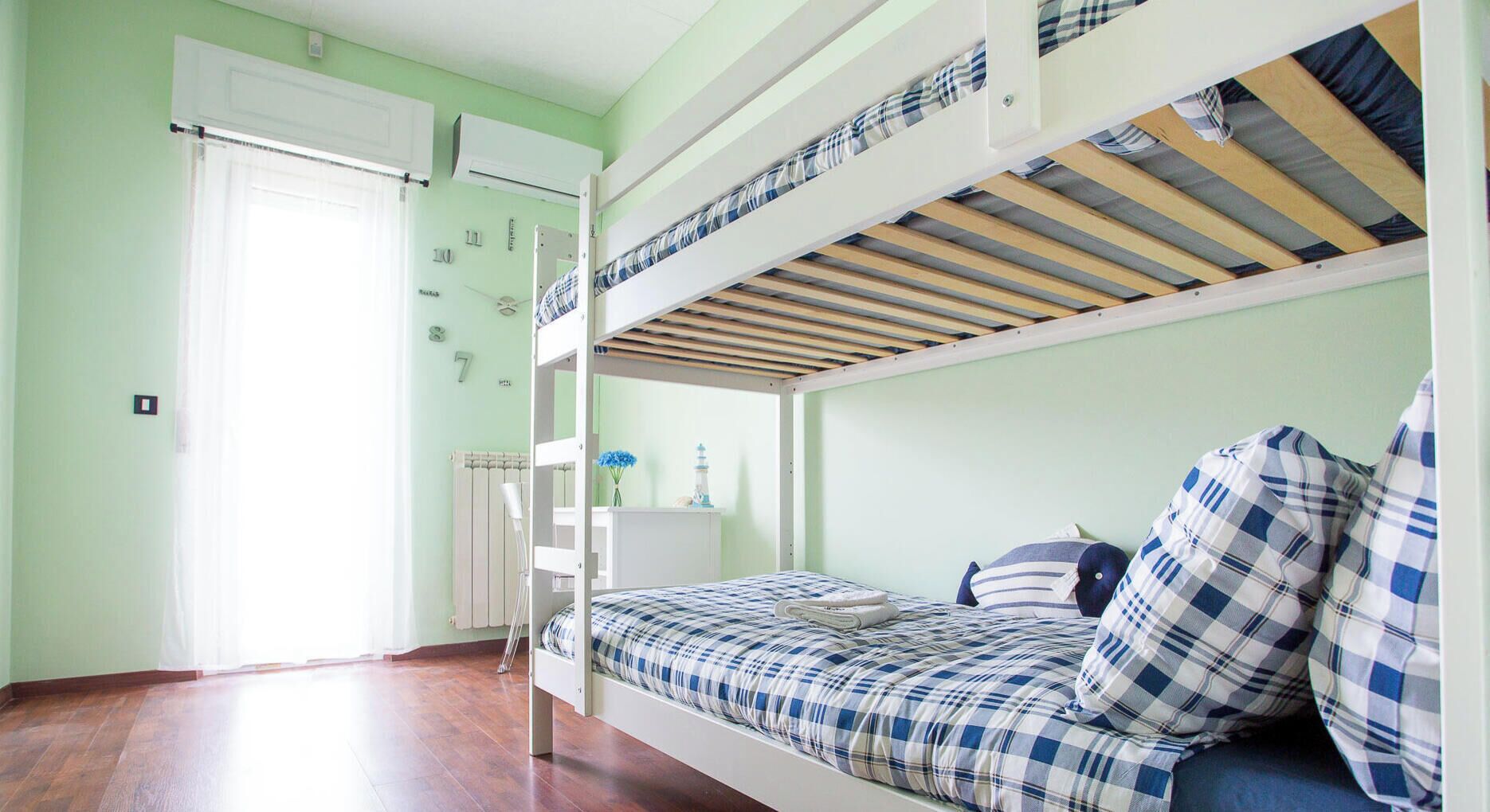 A bunk bed room with a radiator, a window with curtains, and a wall clock.