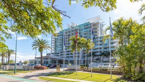 A multi-story hotel with a modern design, featuring balconies, a parking area, and a landscaped garden.