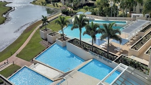 A multi-level swimming pool complex with palm trees, a surrounding lawn, and a view of a river.