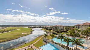 Un campo de golf con un río, una piscina y edificios de hotel.