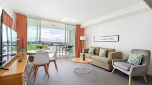 Une chambre d’hôtel moderne dotée d’un balcon, d’un canapé, d’un fauteuil, d’une table basse et d’une télévision.