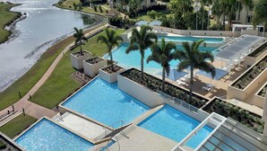 A multi-level swimming pool complex with palm trees, a surrounding lawn, and a view of a river.