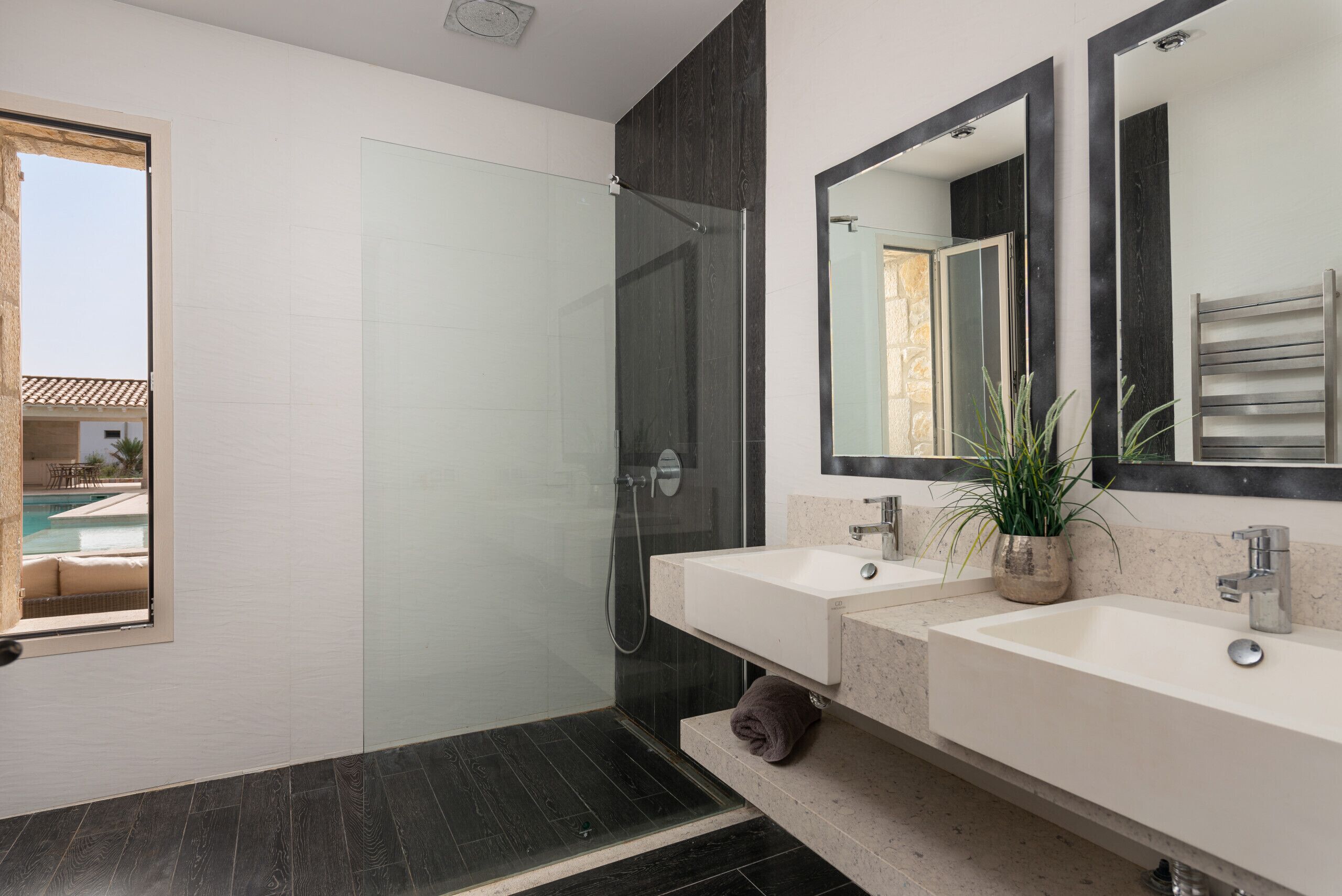A modern bathroom with a glass shower enclosure, dual sinks, and a large mirror.