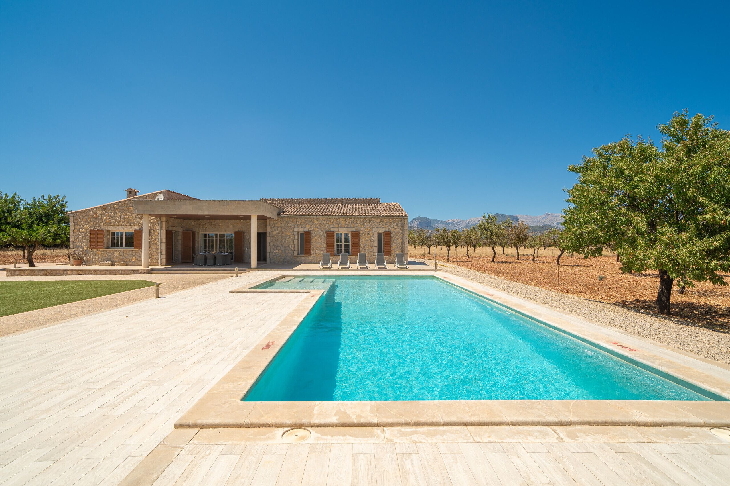 A house with a swimming pool, stone exterior, and a view of mountains.