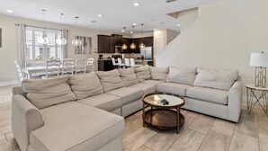 Ein modernes Wohnzimmer mit einer Eckcouch, einem Glastisch und einem Essbereich mit weißen Stühlen.
