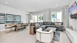 A modern living room with a grey sectional sofa, a white coffee table, and a dining area with a wooden table and chairs.