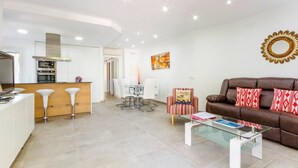 Una sala de estar moderna con un sofá de cuero marrón, una mesa de centro de vidrio y un comedor con sillas blancas.