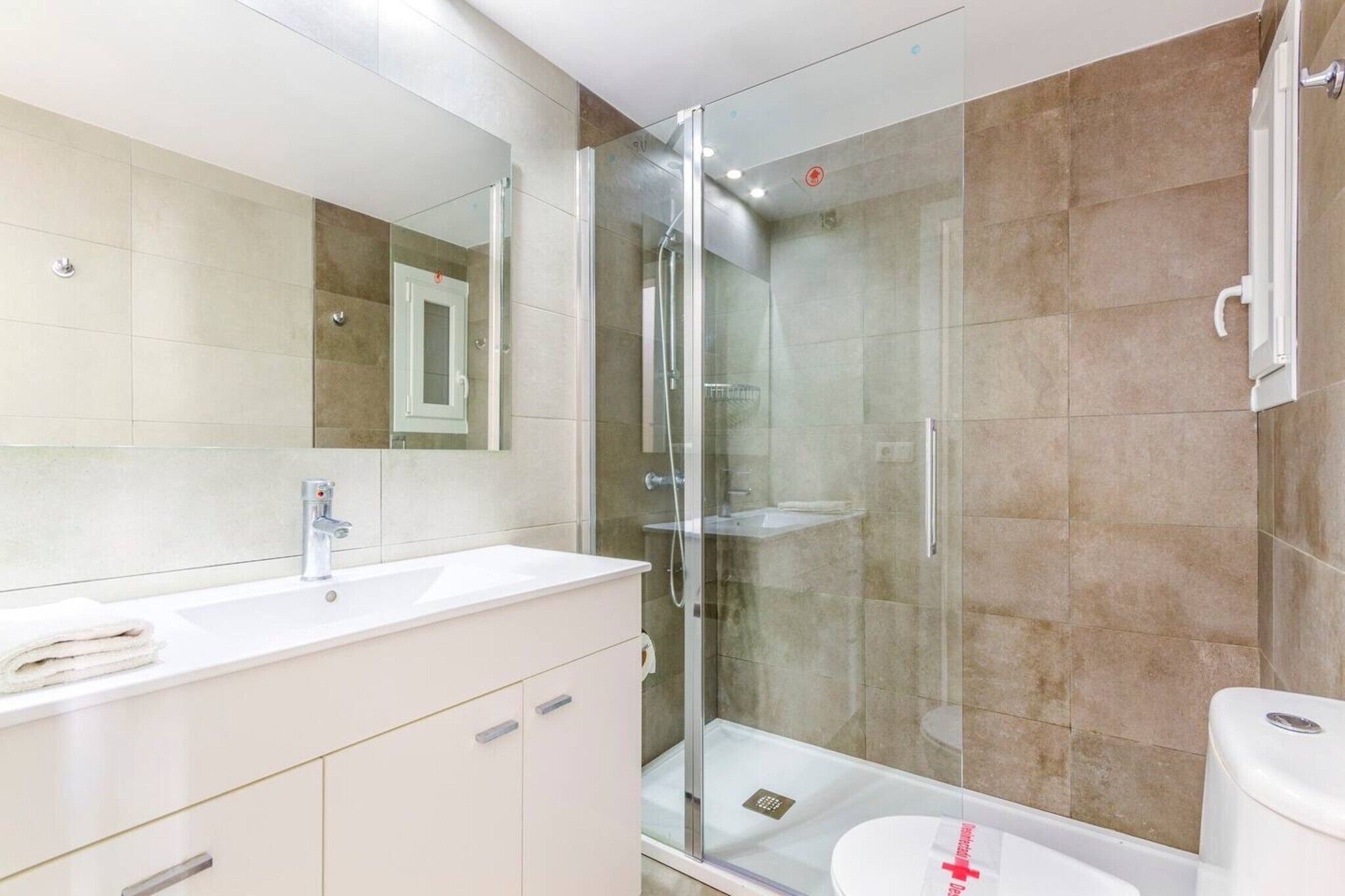 Ein modernes Badezimmer mit einer in Glas abgeschlossenen Dusche, einem weißen Waschbecken und einem großen Spiegel.