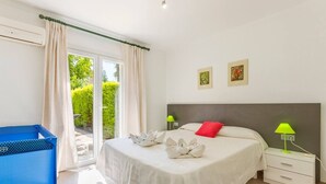 Un dormitorio con una cama, una mesita de noche, una lámpara, un carrito azul y una ventana con cortinas.