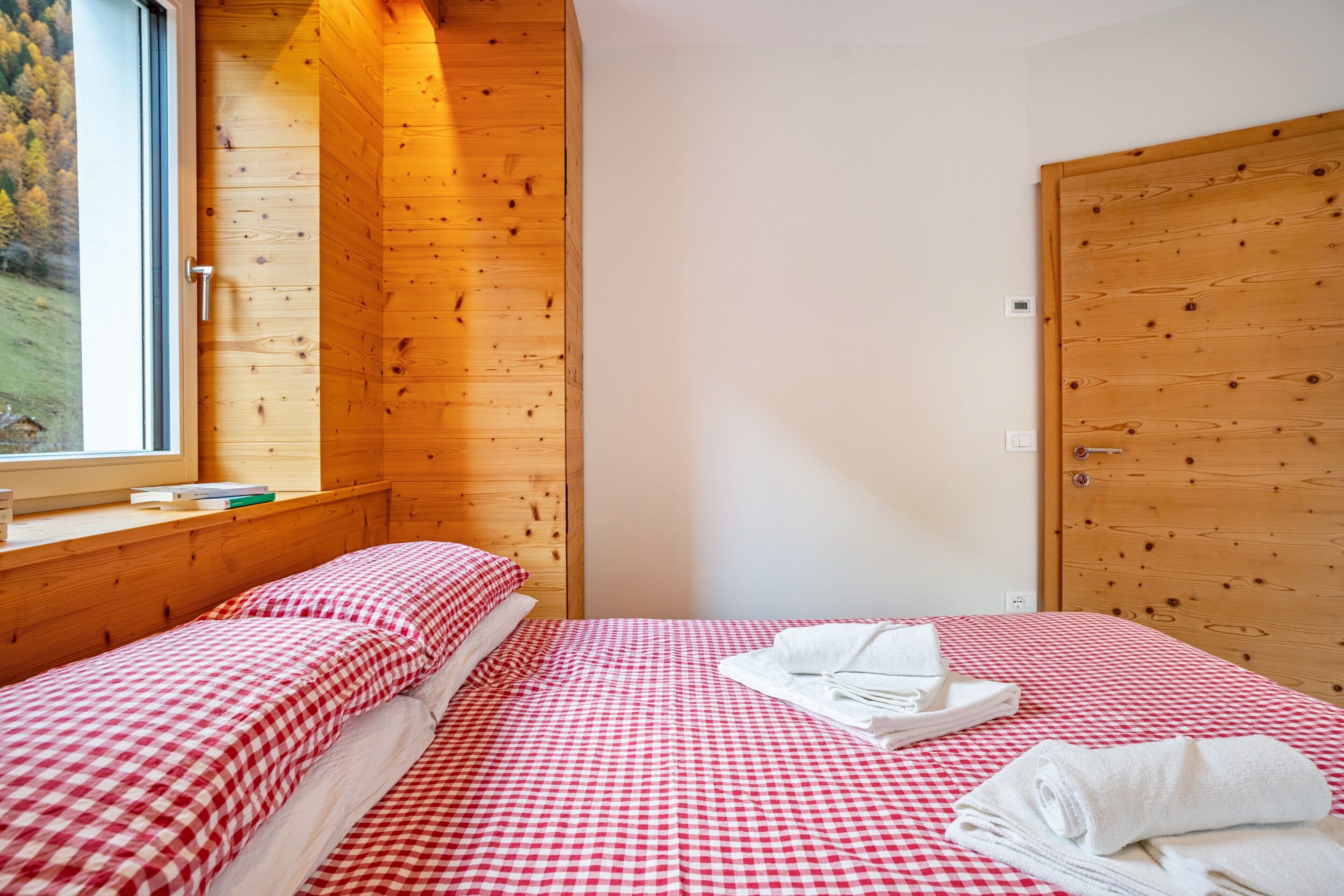 A bedroom with a checkered bedspread, a window with a view of trees, and a wooden door.