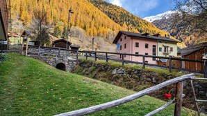 Un village de montagne avec un pont de pierre, des bâtiments rustiques et une vue sur une montagne enneigée.