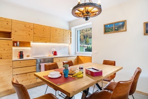 Une cuisine moderne avec des meubles en bois, une table à manger avec des chaises et une vue sur une forêt par la fenêtre.