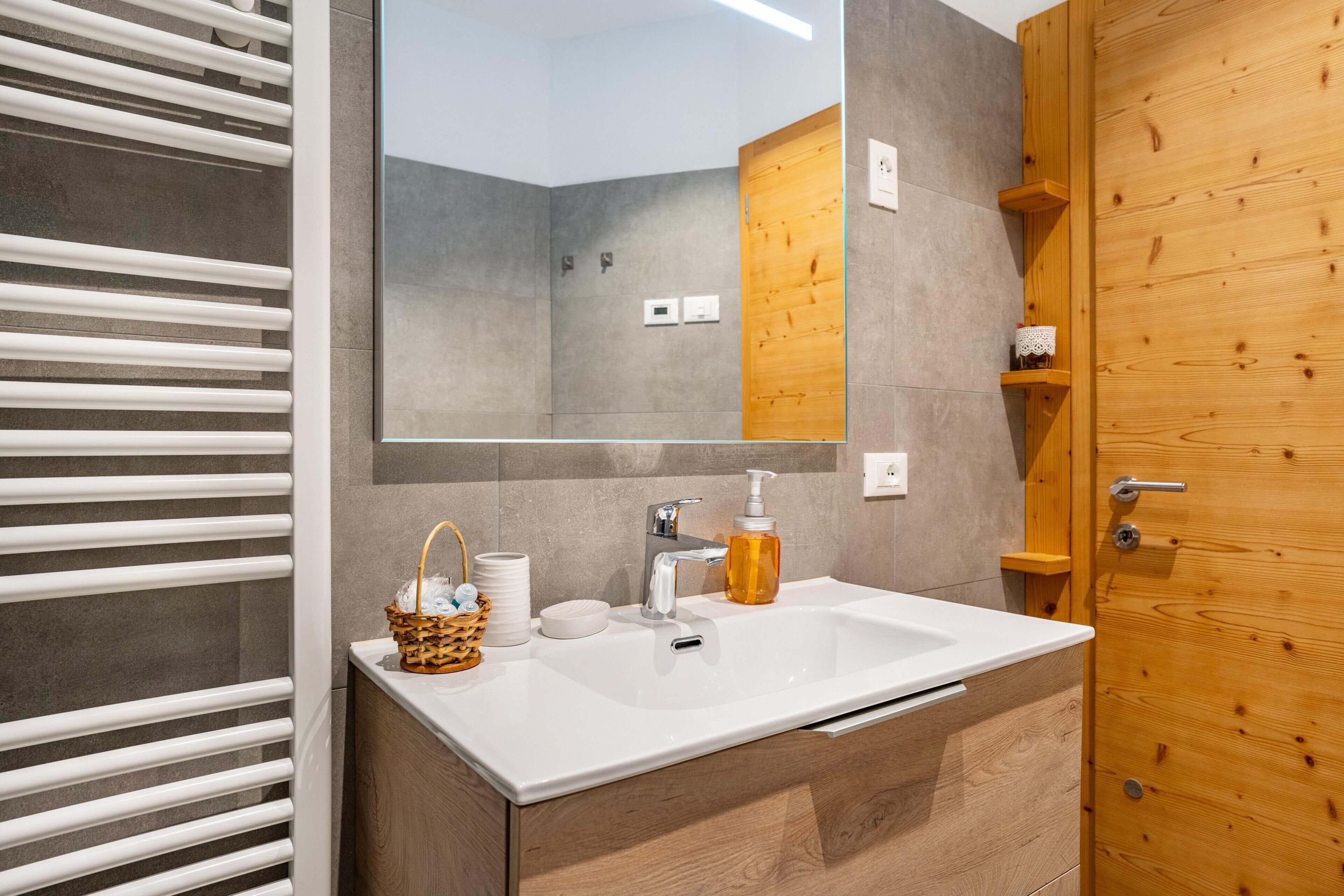 Un bagno con lavandino bianco, mobiletto in legno e uno specchio grande.