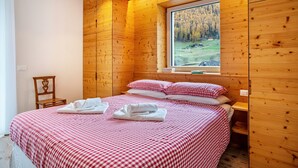 Une pièce aux murs lambrés, avec un lit, une fenêtre donnant sur une forêt et une chaise.