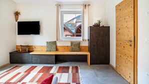 Une chambre moderne dotée d’une grande fenêtre, d’un téléviseur à écran plat, d’un banc avec des coussins, d’un meuble sombre et d’une porte en bois.