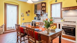 A dining area with a table set for four, a kitchen with a stove and oven, and a yellow wall. - Villa 'Bella Toscana Relax' with Mountain View, Wi-Fi, and Air Conditioning (Monsummano Terme)