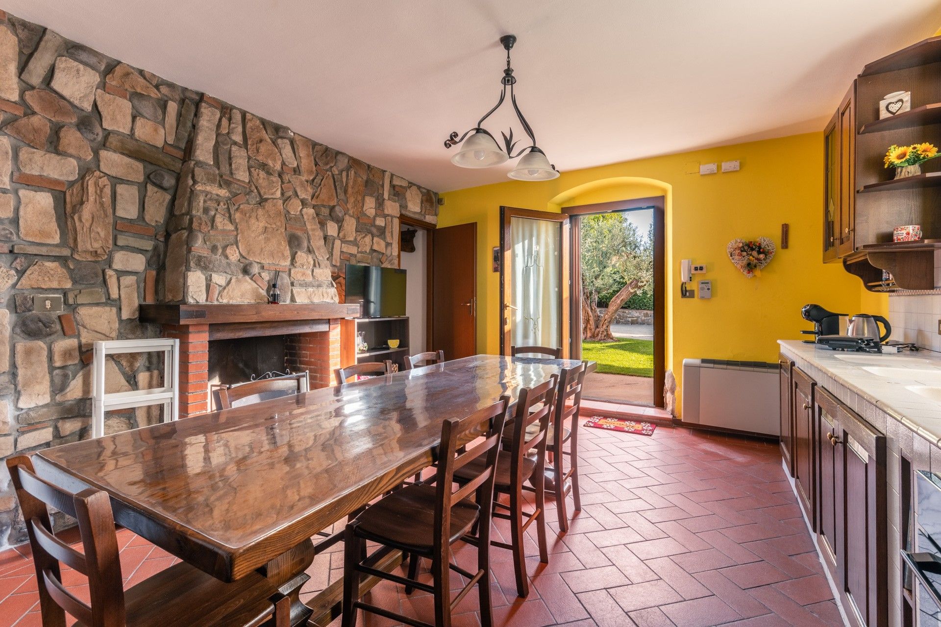 Eine geräumige Küche mit Steinwand, ein Essbereich mit großem Holztisch und Blick ins Freie.