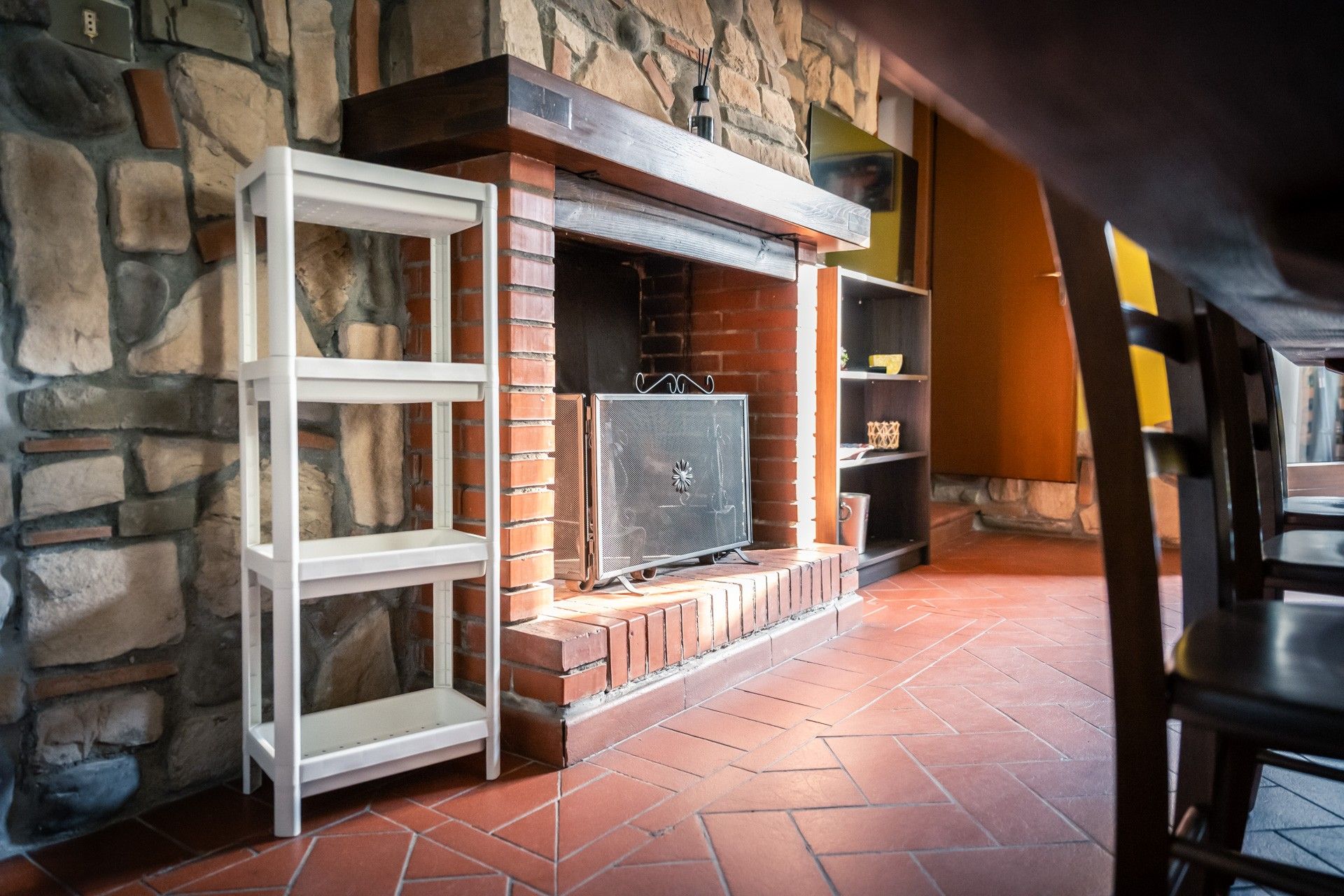 A stone wall with a fireplace, a white shelf, and a black chair.
