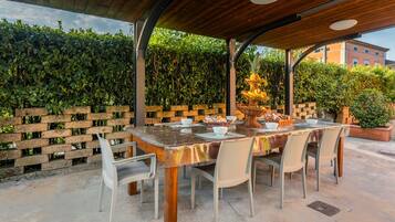 Un patio al aire libre con una mesa y sillas de madera, rodeado por un muro de ladrillo y follaje.