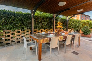 An outdoor patio with a wooden table and chairs, surrounded by a brick wall and greenery.