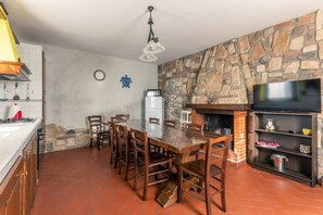 A kitchen with a stone wall, a dining table with chairs, a television, and a fireplace. - Villa 'Bella Toscana Relax' with Mountain View, Wi-Fi and Air Conditioning (Monsummano Terme)