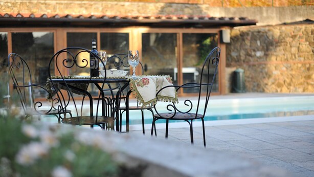 An outdoor dining area with a table and chairs, a pool in the background, and a stone wall. - Villa 'Bella Toscana Relax' with Mountain View, Wi-Fi, and Air Conditioning (Monsummano Terme)