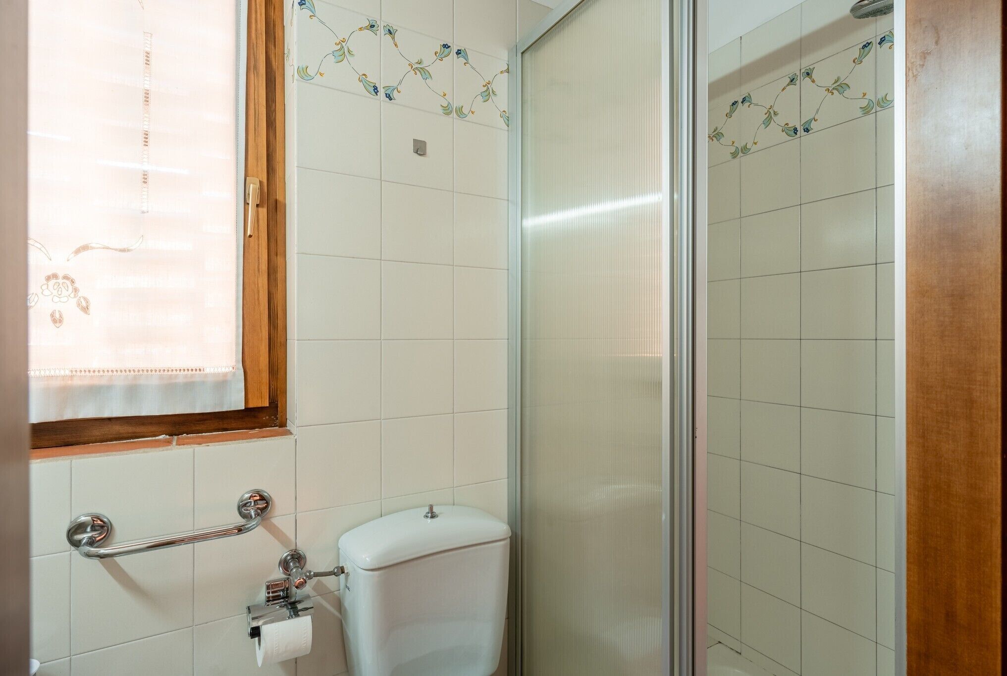 Un baño con inodoro, barra de apoyo y zona de ducha.