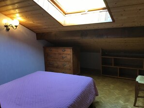 A room with a bed, wooden dresser, and a desk under a sloped ceiling with a skylight.