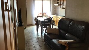 Un salon avec un canapé en cuir, une table à manger avec des chaises, un coin cuisine avec des placards et un réfrigérateur blanc.