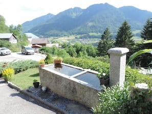 A stone structure with a water feature, surrounded by greenery and a mountainous backdrop.