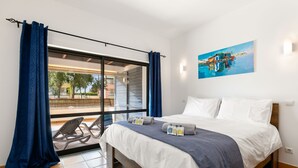 A bedroom with a bed, a painting on the wall, and a view through a window.