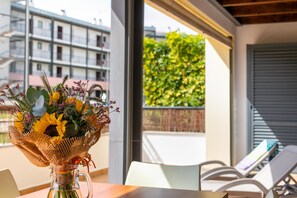 Ein Zimmer mit einem Tisch, einem Blumenstrauß und Blick auf Gebäude und Grünflächen.