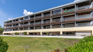 A multi-story building with balconies, a flat roof, and a grassy area in front.