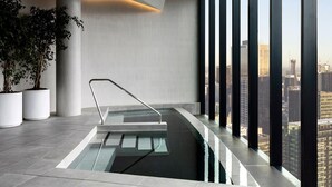 Ein moderner, überdachter Pool mit Glasbarriere und Metallhandlauf, umgeben von großen Fenstern mit Blick auf die Stadt.