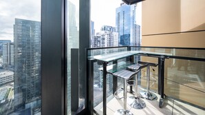 Ein moderner Balkon mit Glastisch und Barhocker, der einen Blick auf die Stadt bietet.
