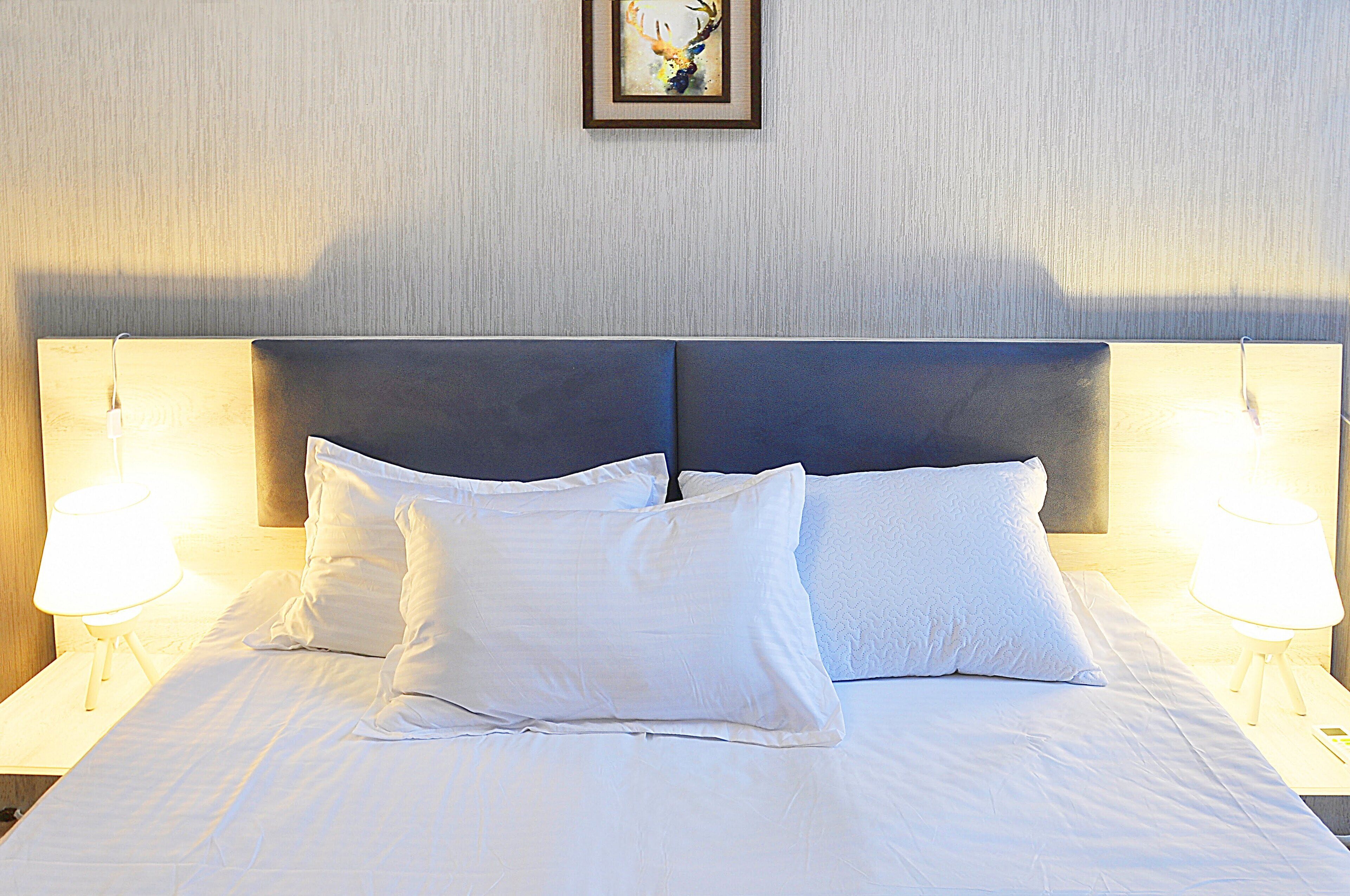 A neatly made bed with white linens and pillows, two bedside lamps, and a framed picture on the wall.
