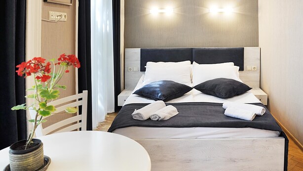A neatly made bed with white and black bedding, a small table with a potted plant, and a modern wall with two wall-mounted lights. - HB apartments Mari Brose (Tbilisi)