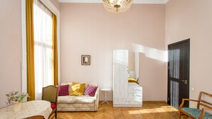 A room with a wooden herringbone floor, a sofa with cushions, a small round table with a white tablecloth, a white cabinet, and a mirror. - HB apartments Mari Brose (Tbilisi)