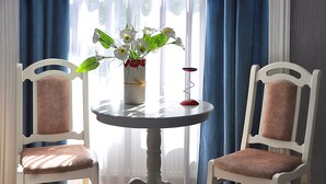A room with two white chairs with cushioned seats, a round table with a vase of flowers, and a red candle holder. - HB apartments Mari Brose (Tbilisi)