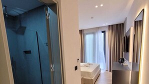 Ett modernt hotellrum med dusch, säng, skrivbord och TV.