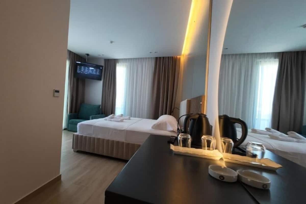 A hotel room with a bed, a desk with a coffee maker, a TV, and a large mirror.