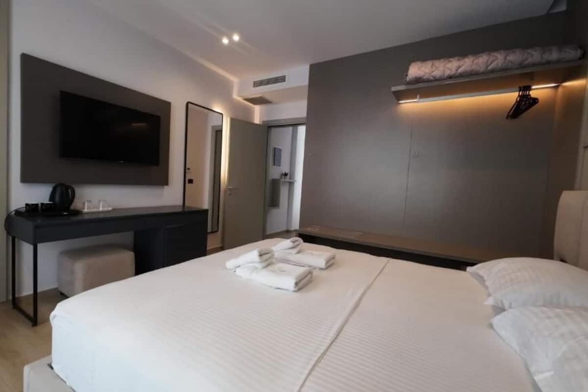 A modern hotel room with a large bed, a desk, a flat-screen TV, and a wardrobe.