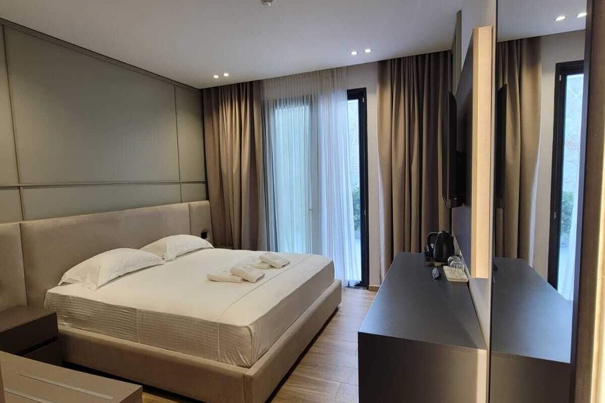 A modern hotel room with a large bed, a bedside table, a built-in TV, and a large mirror.