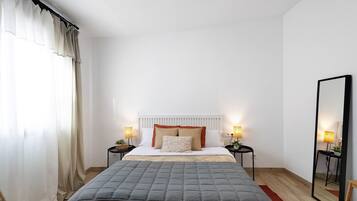 Un dormitorio con una cama, dos mesitas de noche con lámparas, un espejo y una ventana con cortinas.