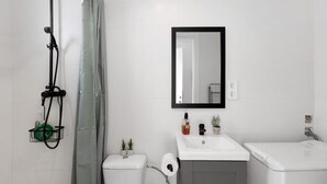 Un baño con ducha, inodoro, lavamanos y espejo.